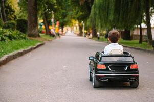 linda chico en montando un negro eléctrico coche en el parque. gracioso chico paseos en un juguete eléctrico coche. Copiar espacio. foto