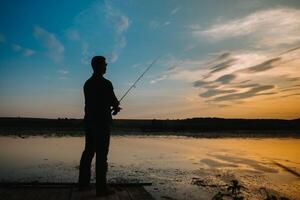 un pescador silueta pescar a puesta de sol. agua dulce pesca, captura de pez. foto