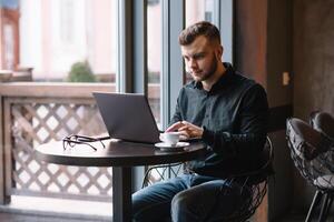 joven exitoso empresario trabajando en un ordenador portátil mientras sentado en café foto