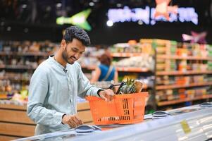 Portrait of handsome young Indian man standing at grocery shop or supermarket, Closeup. Selective Focus. photo