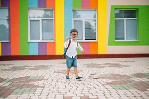 Back to school. Happy smiling boy in glasses is going to school for the first time. Child with backpack and book outdoors. Beginning of lessons. First day of fall photo