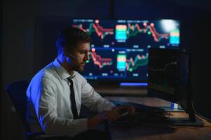 Side view of crypto broker sitting at office table, analyzing market, looking at screen photo