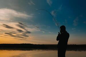 pescador a puesta de sol en el río .hermoso verano paisaje con puesta de sol en el río. pesca. hilado a puesta de sol. silueta de un pescador. foto