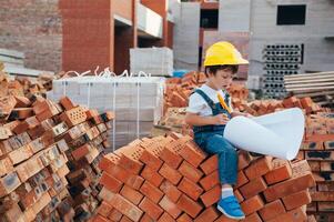 arquitecto en casco escritura alguna cosa cerca nuevo edificio. pequeño linda chico en el edificio como un arquitecto foto