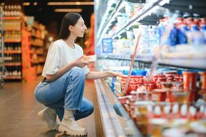 contento joven mujer mirando a producto a tienda de comestibles almacenar. sonriente mujer compras en supermercado foto