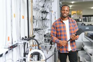 African man in a brown coat chooses a bathroom faucet in a construction supermarket, plumbing repairs in the house photo