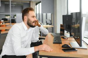 Two Unhappy tired businessman, corporate manager, sits at the workplace, tired from online work, stressed, nervous, massages the bridge of his nose, closed his eyes, experiencing a headache photo