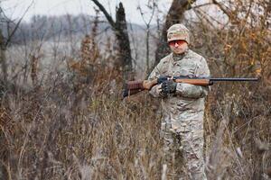 hunting, war, army and people concept - young soldier, ranger or hunter with gun walking in forest photo