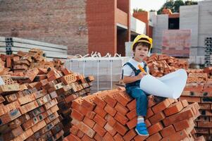 arquitecto en casco escritura alguna cosa cerca nuevo edificio. pequeño linda chico en el edificio como un arquitecto. foto