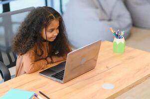 africano americano niña sentado a mesa, utilizando ordenador portátil para en línea lección foto