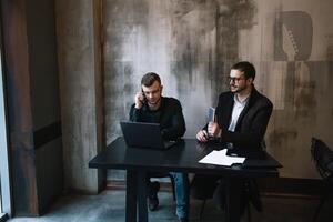 dos empresarios en un oficina sonriente a el cámara mientras trabajando juntos detrás un ordenador portátil computadora. foto