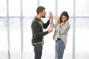 emocional hombre gesticulando y gritos a su esposa, joven Pareja teniendo pelea a hogar. Doméstico abuso concepto foto