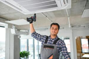 Portrait of young male indian technician repairing air conditioner. Air conditioner repairs. photo