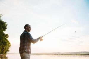 pescador hombre pescar con hilado varilla en un río banco a brumoso brumoso amanecer. pescador con hilado. hilado concepto. foto