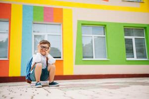 Sad little boy outside of school. Sad schoolboy with books near a modern school. School concept. Back to school. photo