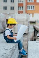 arquitecto en casco escritura alguna cosa cerca nuevo edificio. pequeño linda chico en el edificio como un arquitecto foto