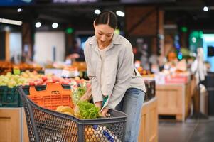 Young woman chooses broccoli, buying vegetables in supermarket. photo