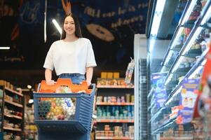 Smiling happy woman enjoying shopping at the supermarket, she is leaning on a full cart photo