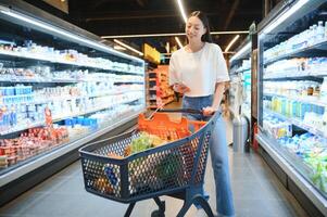 Young satisfied fun woman in casual clothes shopping at supermaket store with grocery cart photo