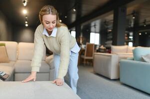 Portrait of young cheerful woman testing sofa in furniture store photo