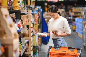 joven sonriente contento mujer 20s en casual ropa compras a supermercado Tienda con tienda de comestibles carro foto