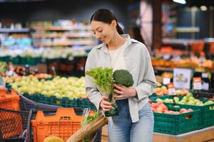 Young woman chooses broccoli, buying vegetables in supermarket. photo