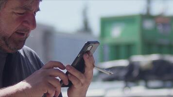 medio Envejecido hombre surf el Internet en móvil teléfono mientras de fumar imágenes. video