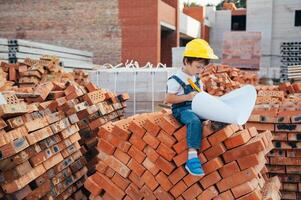 arquitecto en casco escritura alguna cosa cerca nuevo edificio. pequeño linda chico en el edificio como un arquitecto. foto