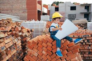 arquitecto en casco escritura alguna cosa cerca nuevo edificio. pequeño linda chico en el edificio como un arquitecto. foto