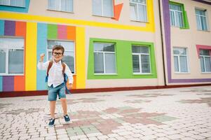 Back to school. Happy smiling boy in glasses is going to school for the first time. Child with backpack and book outdoors. Beginning of lessons. First day of fall photo