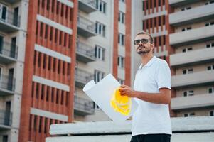 Portrait of an architect builder studying layout plan of the rooms, serious civil engineer working with documents on construction site. photo