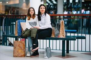 hermosa joven mamá y Adolescente hija son participación compras bolsas, compras en centro comercial. familia compras foto