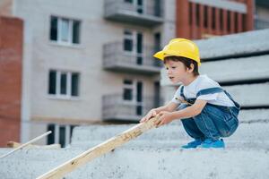 arquitecto en casco escritura alguna cosa cerca nuevo edificio. pequeño linda chico en el edificio como un arquitecto foto