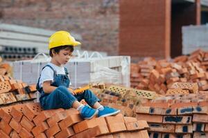 arquitecto en casco escritura alguna cosa cerca nuevo edificio. pequeño linda chico en el edificio como un arquitecto foto