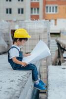 arquitecto en casco escritura alguna cosa cerca nuevo edificio. pequeño linda chico en el edificio como un arquitecto foto