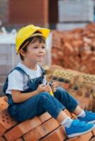 arquitecto en casco escritura alguna cosa cerca nuevo edificio. pequeño linda chico en el edificio como un arquitecto foto