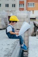 arquitecto en casco escritura alguna cosa cerca nuevo edificio. pequeño linda chico en el edificio como un arquitecto foto