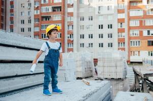 arquitecto en casco escritura alguna cosa cerca nuevo edificio. pequeño linda chico en el edificio como un arquitecto foto