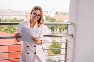 exitoso negocio mujer con financiero documentos en pie cerca un grande ventana en un moderno oficina. foto