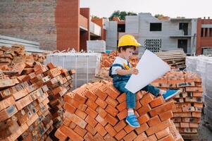 arquitecto en casco escritura alguna cosa cerca nuevo edificio. pequeño linda chico en el edificio como un arquitecto. foto