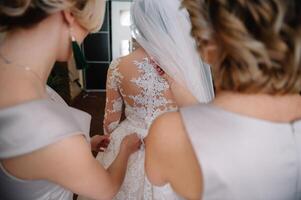 dama de honor preparando novia. dama de honor ayuda sujetar un Boda vestir el novia antes de el ceremonia. lujo nupcial vestir cerca arriba. mejor Boda Mañana foto