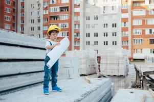 arquitecto en casco escritura alguna cosa cerca nuevo edificio. pequeño linda chico en el edificio como un arquitecto foto