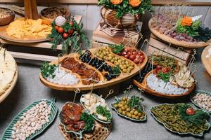 Antipasti board with various cheese and meat snacks with hummus and olives on wooden round board on black table photo