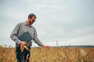 Agronomist holds tablet touch pad computer in the soy field and examining crops before harvesting. Agribusiness concept. agricultural engineer standing in a soy field with a tablet. photo