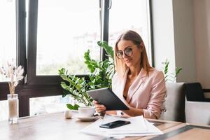 Young smiling businesswoman drinking coffee and using tablet computer in a coffee shop. photo