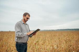 Agronomist holds tablet touch pad computer in the soy field and examining crops before harvesting. Agribusiness concept. agricultural engineer standing in a soy field with a tablet. photo