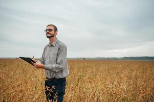 Agronomist holds tablet touch pad computer in the soy field and examining crops before harvesting. Agribusiness concept. agricultural engineer standing in a soy field with a tablet. photo