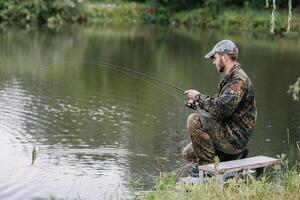 pescar en rio.a pescador con un pescar varilla en el río banco. hombre pescador capturas un pescado pesca del lucio, hilado carrete, pez, breg ríos - el concepto de un rural escapar. artículo acerca de pescar foto