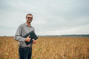 Agronomist holds tablet touch pad computer in the soy field and examining crops before harvesting. Agribusiness concept. agricultural engineer standing in a soy field with a tablet. photo
