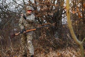 A male hunter with a gun while sitting takes aim at a forest. The concept of a successful hunt, an experienced hunter. Hunting the autumn season. The hunter has a rifle and a hunting uniform photo